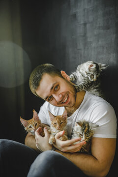 the guy sits on the floor leaning against the wall among the maine coon cats. male cat lover playing with cats sitting on the floor. incredible beautiful cats and model in T-shirt