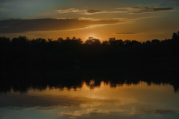 Sunset and tree silhouette under forest lake. bright fire orange dawn or sunset