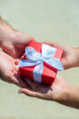 female hands accept a gift from male hands. on the street they give a red box, a white bow. holiday concept, surprise