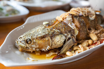 Deep Fried Sea Bass topped with fish sauce, Peanut and chili. serving on white plate. Thai traditional food.