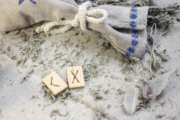 Scandinavian wooden rune Kenaz and Gebo on a rough linen cloth with amethyst crystalline, rock crystal and dried wormwood