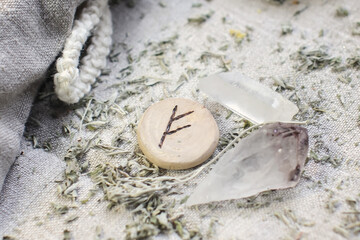 Scandinavian wooden rune Fehu, Fe, Feoh on a rough linen cloth with amethyst crystalline, rock crystal and dried wormwood