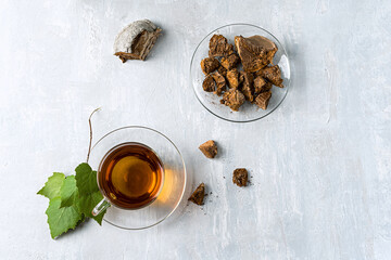 Chaga mushroom drink in a glass cup and teapot. Trendy healthy birch mushrooms. View from above. Horizontal orientation Light gray stone background.