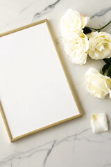 Gold foto frame mock up ,cream roses top view on marble background table. copy space. Lifestyle flat lay