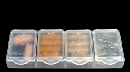 Tablets and capsules are in a white plastic box to help you take the medication on time, isolated on a black background. 