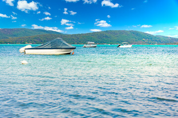 Boats parked on the sea, mountains and green trees on background during sunny day under blue sky with clouds in Greece