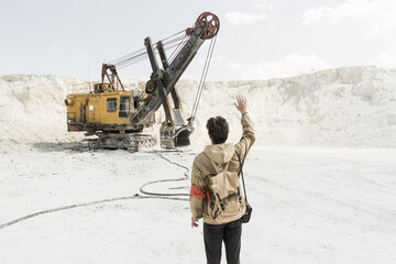 the traveler stands in front of a large excavator. white sand pit. Stalker in the world of post-apocalypse.