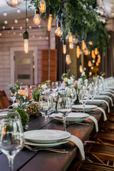 Wedding reception table with Edison bulbs and decor of greenery. Decoe. Wedding table setting