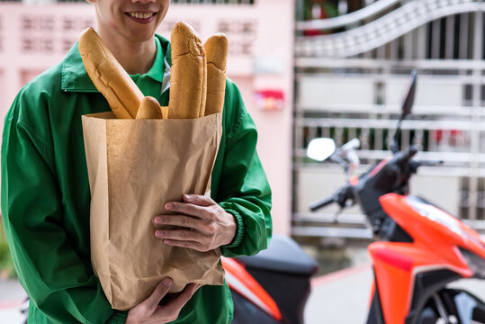 Smiling delivery man hold bakery bag with motorbike