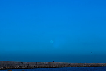 Naklejka na ściany i meble view The Dam of Punta Riso, Brindisi. Colorful blue sky with cloud and bright full moon on seascape to night. Serenity nature background, outdoor at nighttime