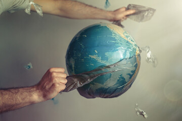 Men's hands tear off a plastic bag from the globe of planet Earth. The concept of environmental...