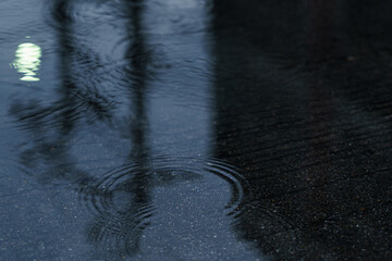 Rain drops rippling in a puddle. the street light refected in the puddle of water