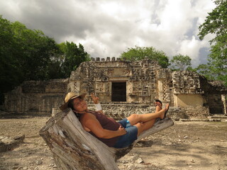 Fototapeta premium Mujer turista posa con un sombrero recostada en tronco con una ciudad Maya detras