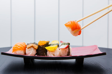 Salmon sushi held by chopstick with assorted sushi