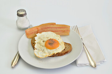 Sandwich with Bacon and fried Egg with Salt and Pepper on white Plate, closeup, isolated on white Background