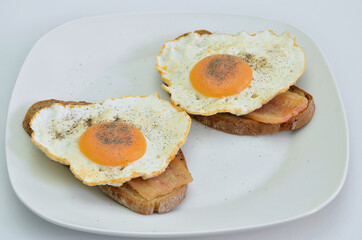 Two Sandwiches with Bacon, fried Egg, Salt and Pepper on white Plate,  closeup isolated on white Background