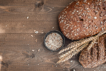 The bakery, several different fresh loaves of bread with a crisp crust, sprinkled with seeds and sesame seeds on a wooden background with boils of wheat.