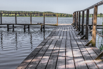 Obraz premium Wooden pier on the lake. Rural landscape. Place of power. The beauty of the countryside. Pacification of nature. An ideal place for meditation. Boardwalk pier for fishing.