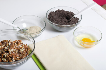 Ingredients for making puff pastry curls stuffed with poppy and walnut. Are laid out on a white table top.