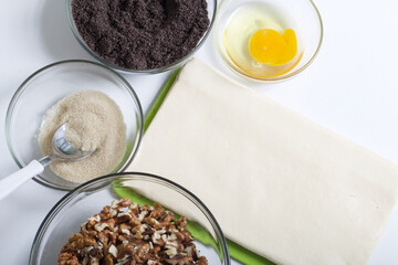 Ingredients for making puff pastry curls stuffed with poppy and walnut. Are laid out on a white table top.