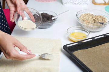 A woman sends puff pastry with sugar. For making puff pastry curls with poppy and walnut filling. Nearby on the table are ingredients and tools.