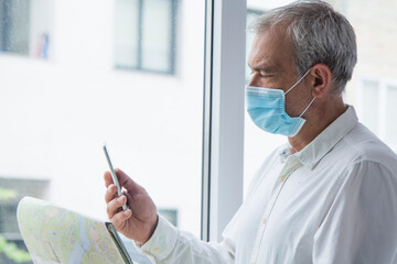 man in medical mask with a world map in his hand and in the other the mobile phone, concept of travel in the new normal