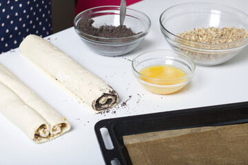 Puff pastry rolled into a tube. Filled with poppy and walnuts. For making curls. Nearby on the table are ingredients and tools.