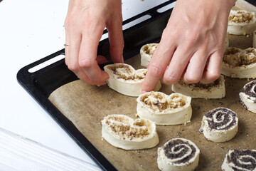 A woman lays curls filled with poppy and walnuts on a baking sheet. Nearby on the table are ingredients and tools.