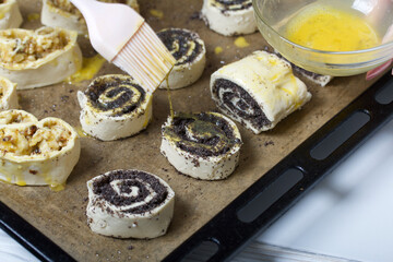 A woman smears an egg on curls stuffed with poppy and walnuts. For baking.