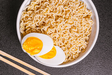 noodles in a plate with sesame seeds bamboo sticks, boiled eggs on a black table close-up. flat ley. copy space.