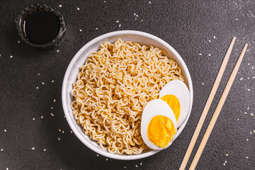 noodles in a plate with sesame seeds and soy sauce, bamboo sticks, boiled eggs on a black table close up. flat ley. copy space
