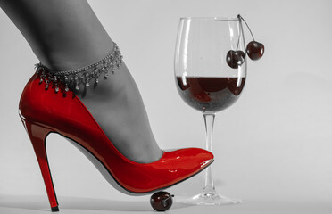 female feet with chain decoration in patent leather red stiletto heels and wine glass