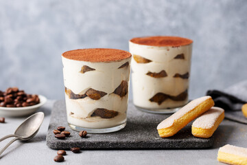 Tiramisu dessert in glass on cutting board. Grey background. Close up.