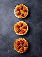 Pecan pies, mini tarts. Traditional Thanksgiving dessert. Dark background. Top view.