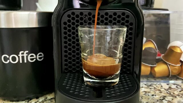 Process of making coffee by coffee machine into glass transparent cup, espresso coffee coming out from an automated coffeemaker machine. Beverage drink for breakfast. Home making hot Espresso. 