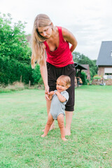 Mother helping baby learning to walk in garden