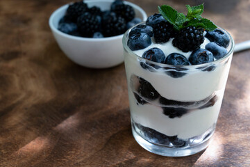 Fototapeta na wymiar Cottage cheese dessert with blueberries, blackberries and mint in a transparent glass glass. On a wooden background. Yummy.