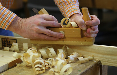 Zwei H&auml;nde halten einen Hobel und hobeln Holzsp&auml;ne