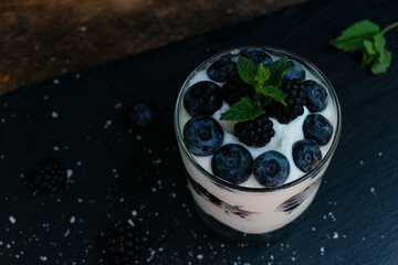 Cottage cheese dessert with blueberries, blackberries and mint in a transparent glass glass. On a black board. Yummy.