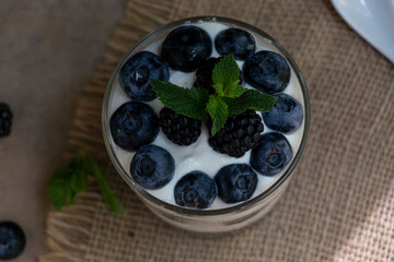 Cottage cheese dessert with blueberries, blackberries and mint in a transparent glass glass. On a burlap napkin and on a wooden background. Delishious.