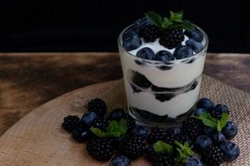 Cottage cheese dessert with blueberries, blackberries and mint in a transparent glass glass. On a burlap napkin and on a wooden background. Delishious.