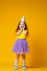 Happy Birthday! little girl in festive hat on her birthday on yellow background.