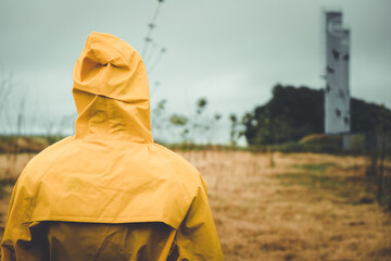 a girl in a yellow raincoat in a cloudy rainy looks straight, hair develops in the wind