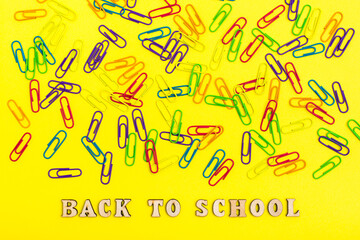 Back to school. Colored paper clips on a yellow background randomly and phrase in wooden letters