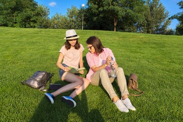 Mom and daughter teenager student together sitting on the green lawn