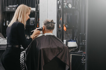 Woman barber cutting hair to an aged bearded man. Elderly man in barbershop concept.