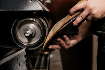 Male shoemaker repairing sole of shoe on grinding machine. Cobbler at work.
