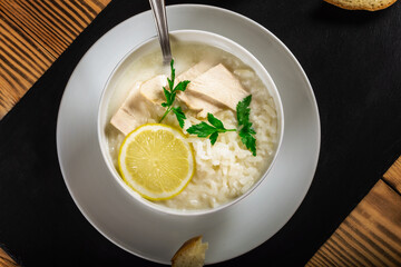 Chicken soup with lemon, egg yolks, parsley and rice. low key. Black background.