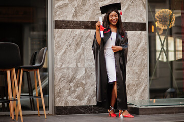 Young female african american student with diploma poses outdoors.