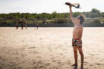 Young man, wearing a swimsuit, throwing a toy plane or glider on the beach in summer. Background or wallpaper with copyspace.